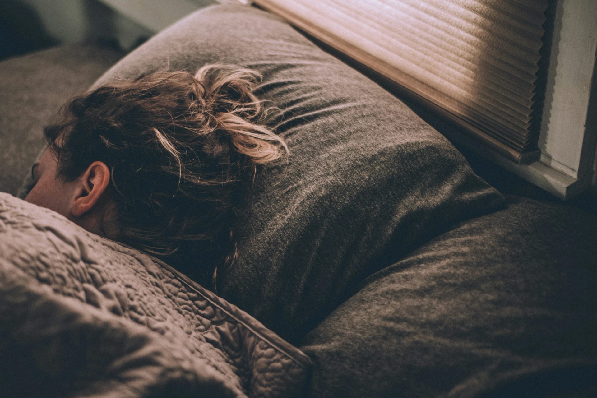person journaling in dim evening light with phone charging across the room and sleep tracker on wrist